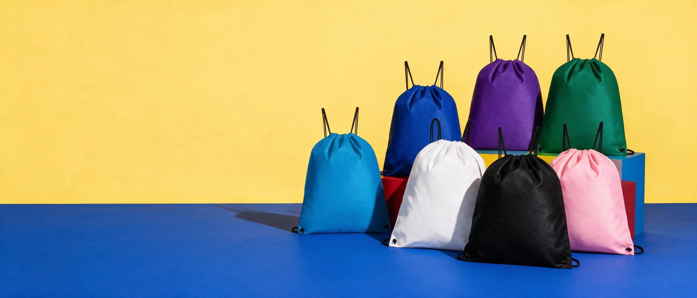 Bolsas-mochila de colores con cordón sobre cubos, fondo amarillo y piso azul