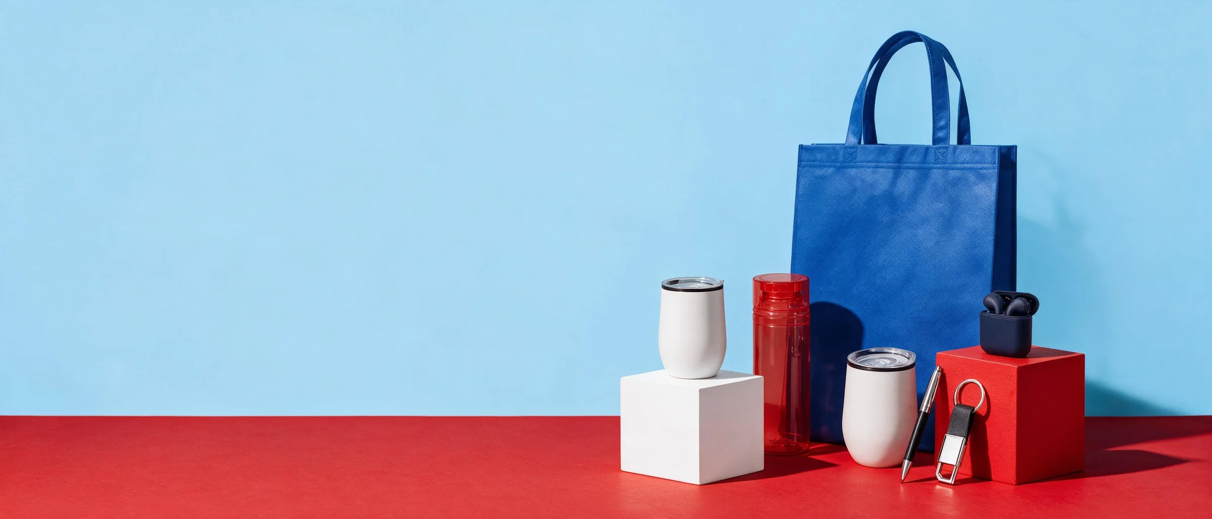 Kit con bolsa azul, termos blancos, cilindro rojo, estuche de audífonos, pluma y llavero sobre cubos rojos y blancos